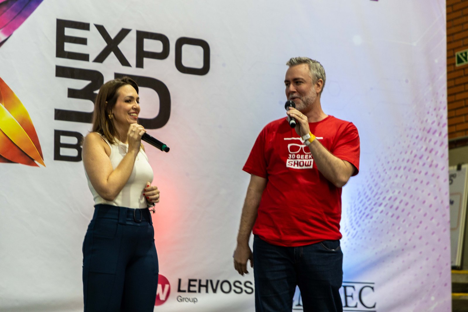 Apresentadores no palco principal da Expo3DBR 2026 com o logotipo do evento ao fundo.